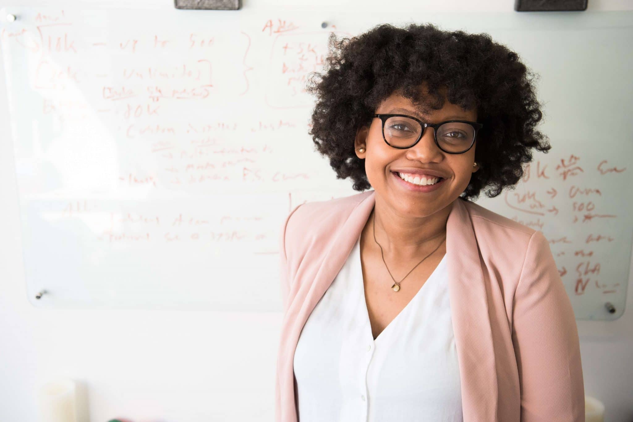 An African American teacher smiling in front of her classroom board filled with equations