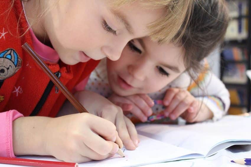 Two young girls starting to learn social skills and how to write from a young age.