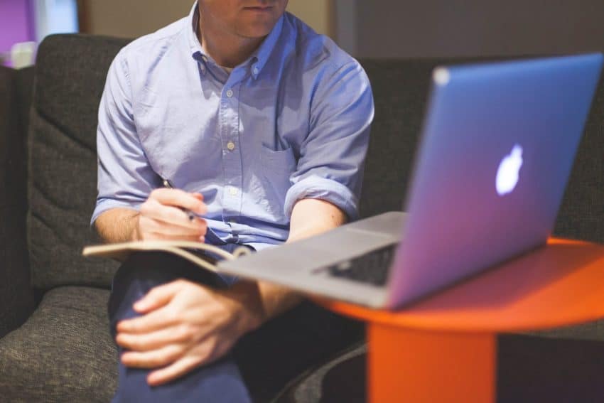 Man on sofa with notebook on lap and laptop on desk